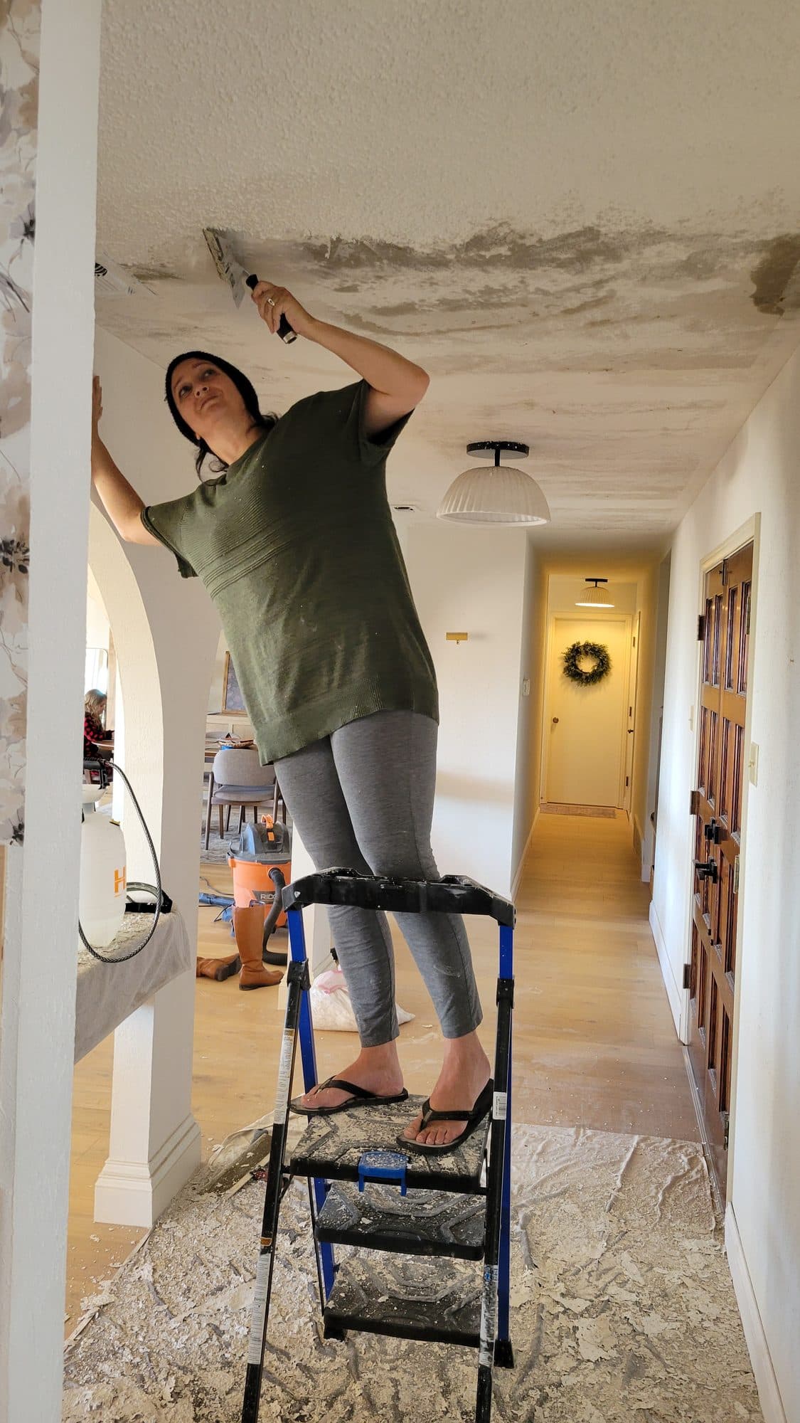 Savana on a step ladder scraping a popcorn ceiling during a renovation