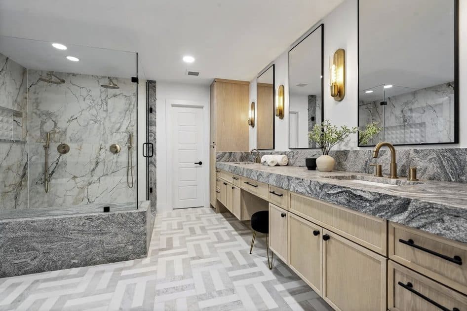 Primary bath with stone shower, double vanity, and herringbone tile floor