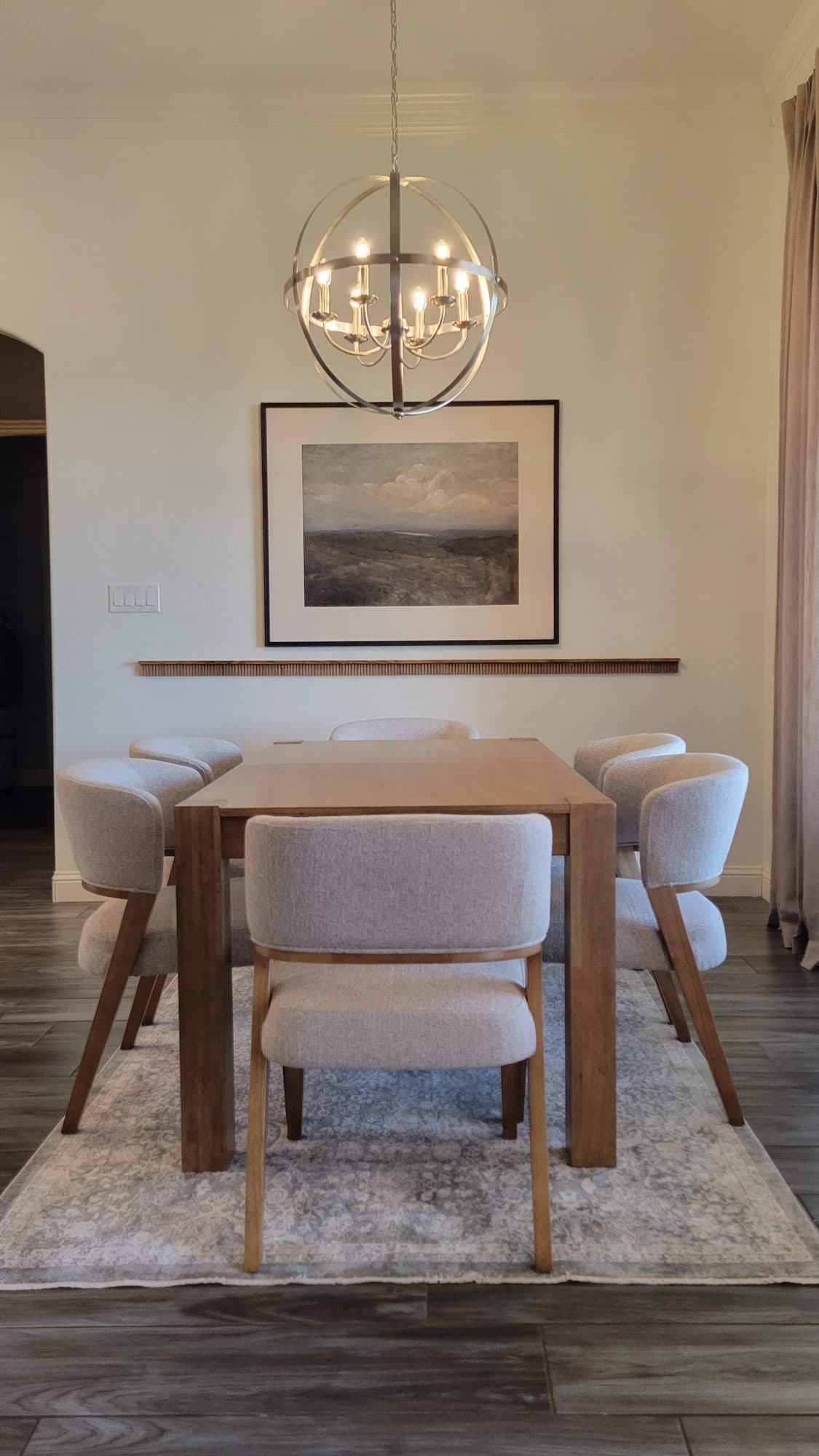 Wood dining table with upholstered chairs under an orb chandelier